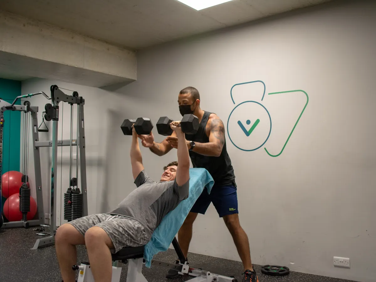Personal trainer spotting a client on a dumbbell press at Move Better Studio in Sliema